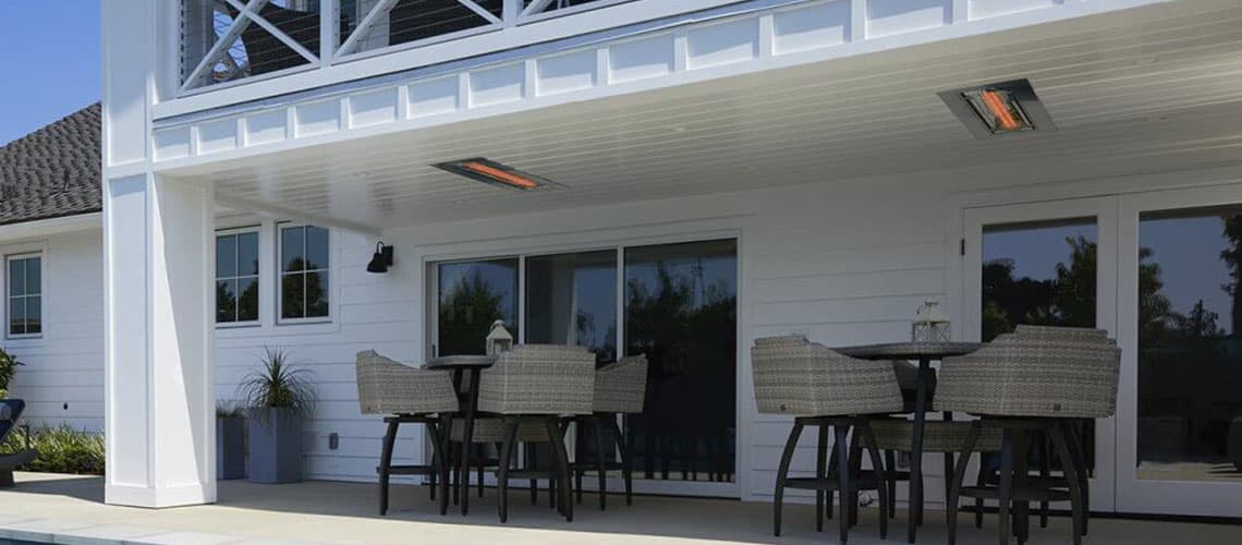 Two Electric Patio Heaters Recessed into the Ceiling of a Covered Patio Over Two Sets of Outdoor Bar Height Tables and Chairs in a Backyard
