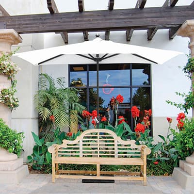 specialty umbrella over a bench with red flowers in the background